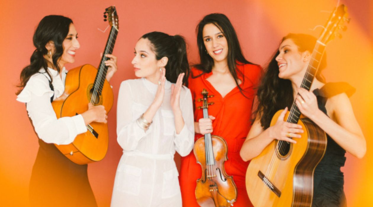 The four members of Las Migas, an all female flamenco quartet, pose in front of a yellow and orange background.